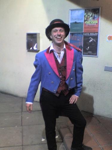 Andrew poses in a bright blue tailcoat, with hot pink lapels, and a bowler hat.