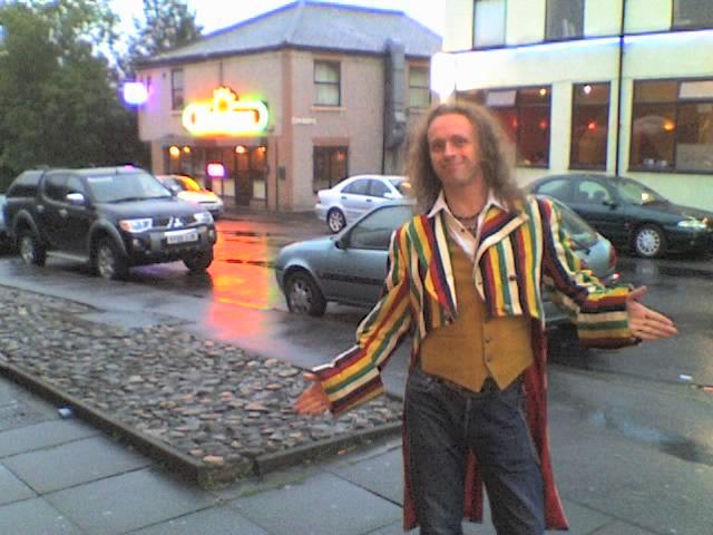 Andrew poses in a multi-coloured stripey tailcoat, with open arms