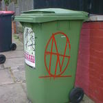 A red monogram spray-painted on a green wheelie bin.