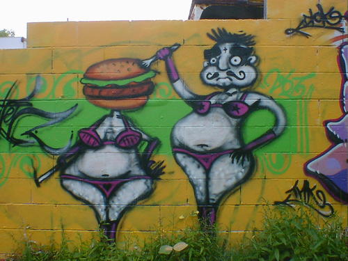 Fat woman in bikini with a hamburger for a head. A fat man sticks a fork in it.
