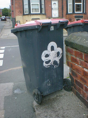 A five-petalled flower painted on a wheelie bin.