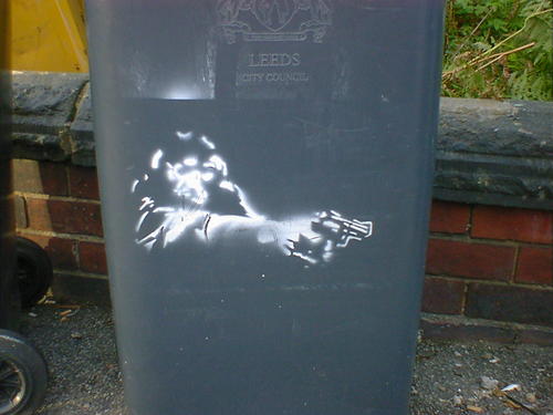 Stencil art on a wheelie bin. A monkey aiming a revolver, cop-show style