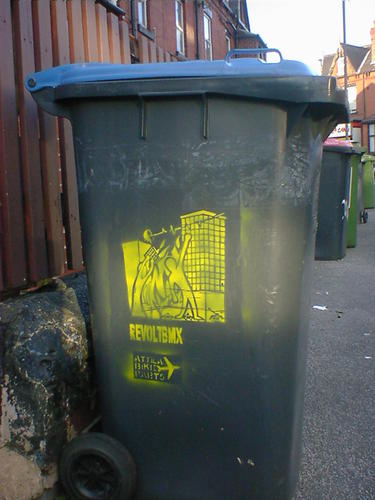 Wheelie bin with stencil art of a mob uprising, advertising Attila Bike Parts.