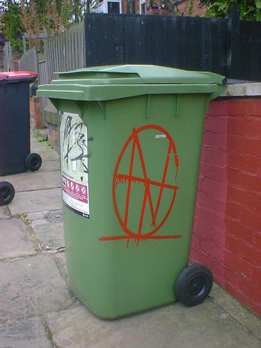 A red monogram spray-painted on a green wheelie bin.