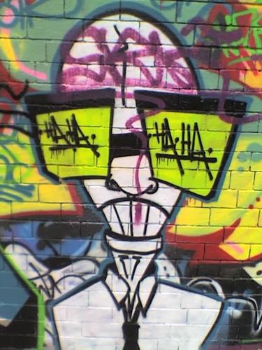 Graffiti art - a bald scientist with big green spectacles. The lenses say HA HA.
