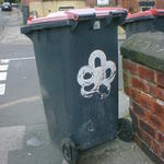 A five-petalled flower painted on a wheelie bin.