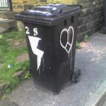 A wheelie bin painted with a lightning bolt on one side and a heart on another.