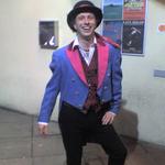 Andrew poses in a bright blue tailcoat, with hot pink lapels, and a bowler hat.