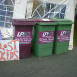 A sign for lost kids is leans next to 3 wheelie bins.